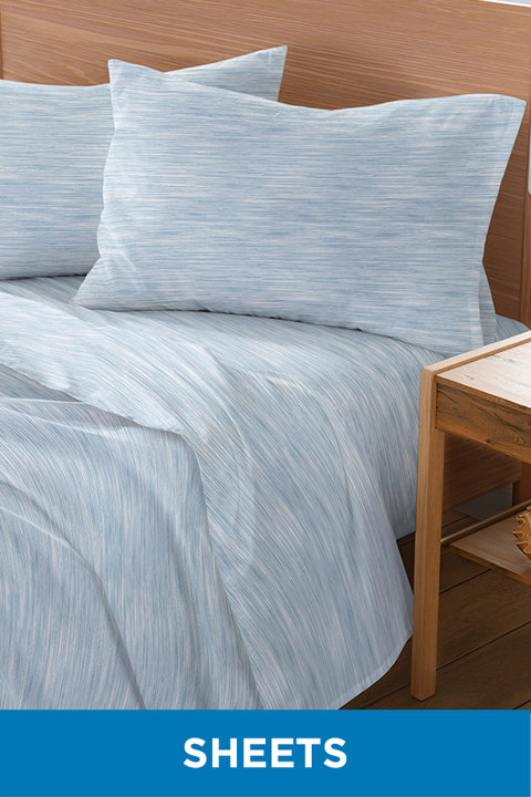Light blue and white heathered pattern bed sheets on a bed with a wooden headboard and nightstand, labeled Sheets.