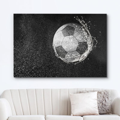 Black and white canvas wall art featuring a soccer ball with a water splash effect, displayed above a beige sofa.