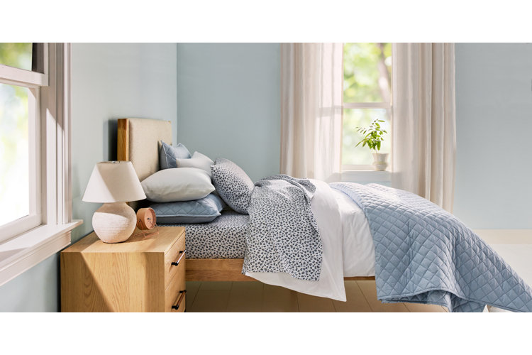 Boho dining room styled bedroom with light blue walls, a wood nightstand, and blue quilted and floral patterned bedding