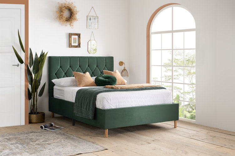 green bed frame with white bedding in a bedroom with a big window, banana plant, and wall art