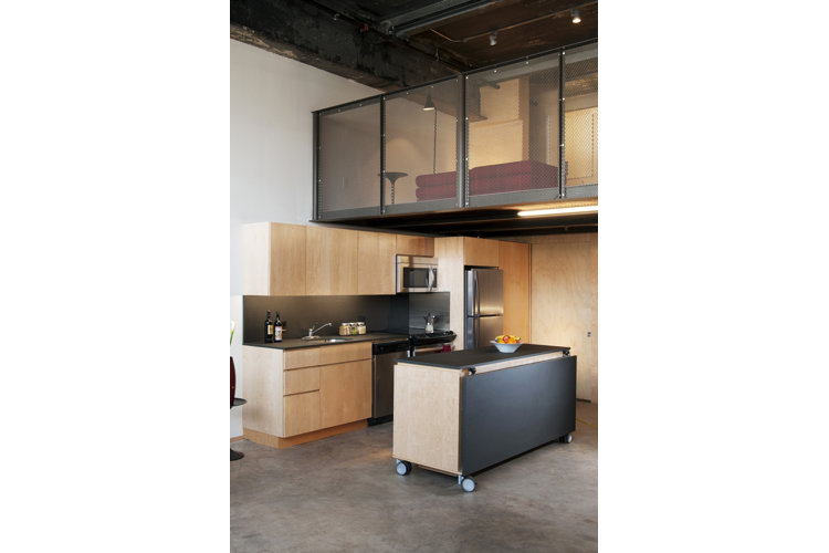 A modern kitchen in a loft styled home with a rolling kitchen island with a fold out counter top. 