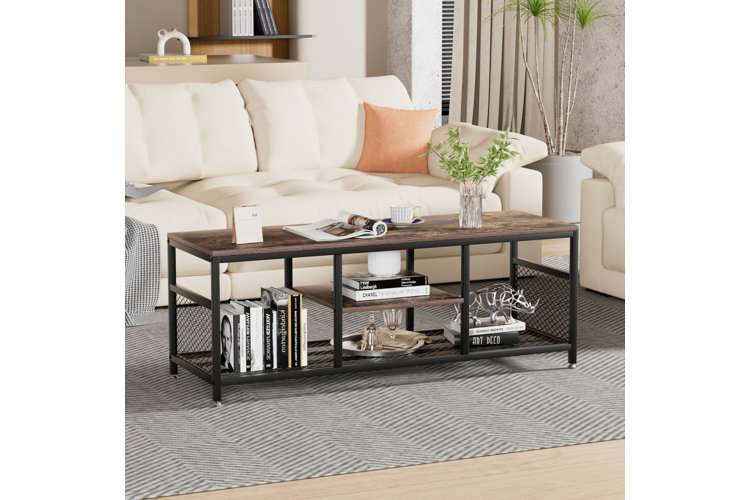 a brown wood and black metal coffee table with books on art, a vase with plants, a calendar, mug, and animal sculpture
