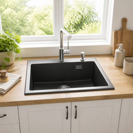 Matte black kitchen sink with a chrome tap set into a light wood worktop in front of a window.