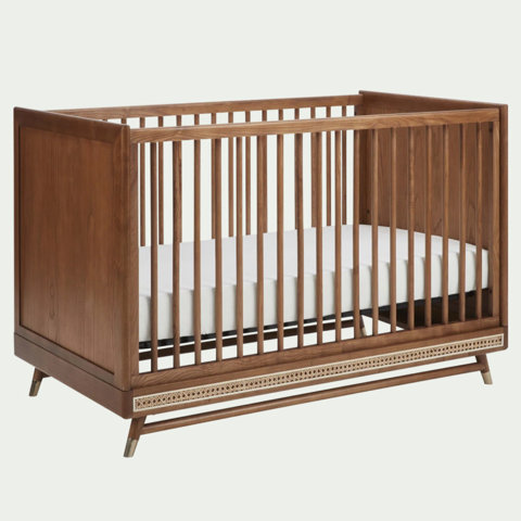 Mid-century modern wooden crib with spindle slats and decorative cane detailing on a neutral background.