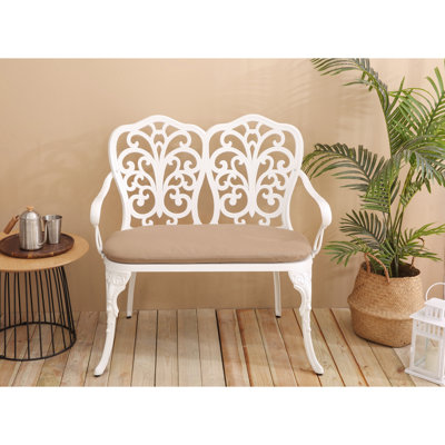 Banc de patio en aluminium moulé, orné de roses et d'un coussin blanc, pour une terrasse ergonomique et attrayante sur la pelouse.