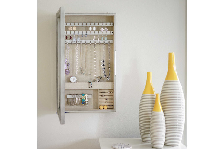 Wall mounted jewelry organizer with earrings necklaces and bracelets next to three vases