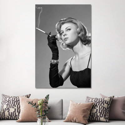 Femme des années 1960 sensuelle dans une robe de soirée noire avec un long gant noir et un fumoir à cigare par Vintage Images - Photographie sur toile tendue