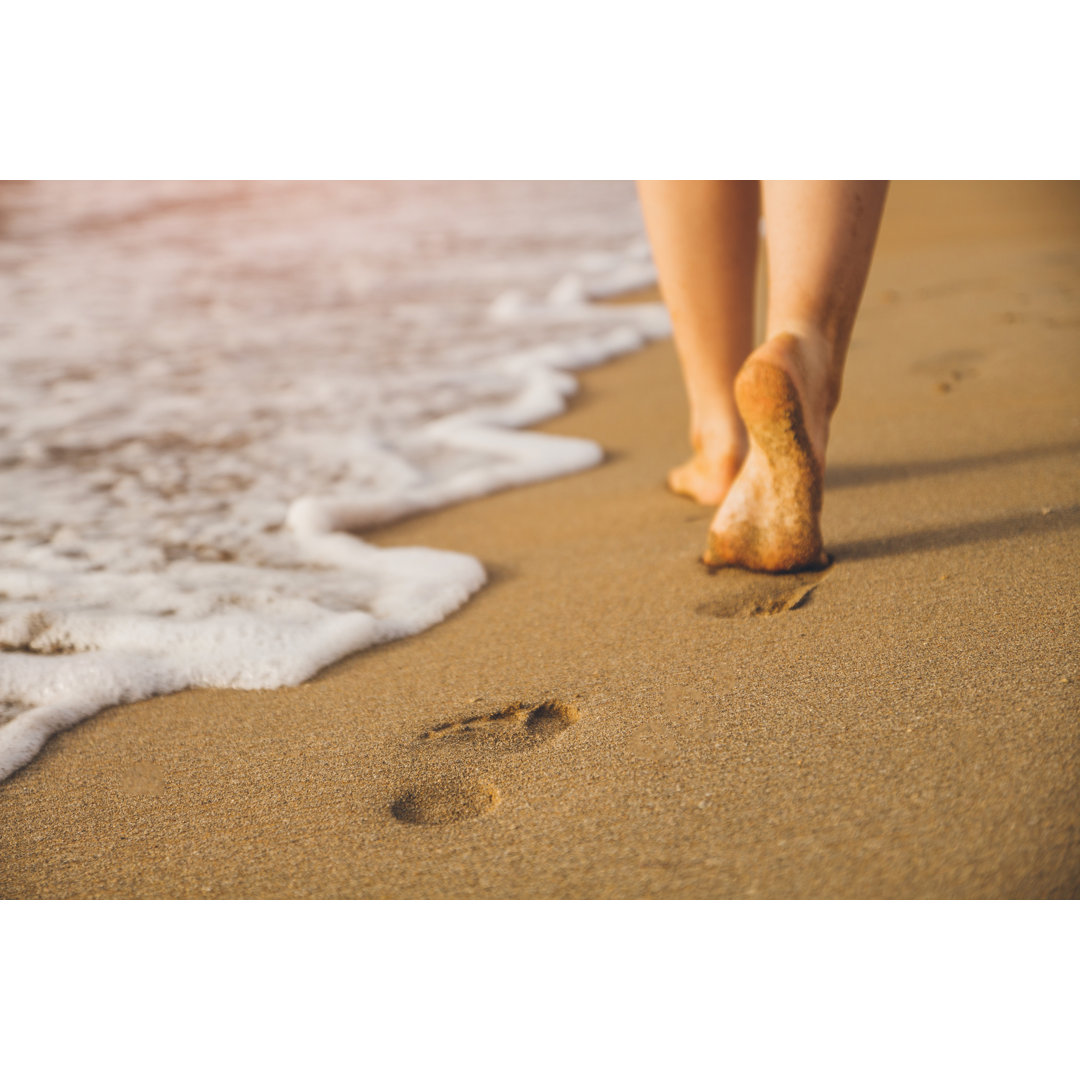 Leinwandbild Frau geht auf Sandstrand und hinterlässt Fußabdrücke im Sand