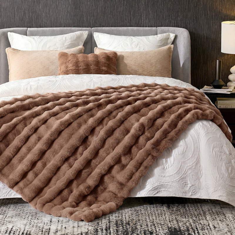 Brown faux fur throw blanket with a bubble wave texture draped over a bed.