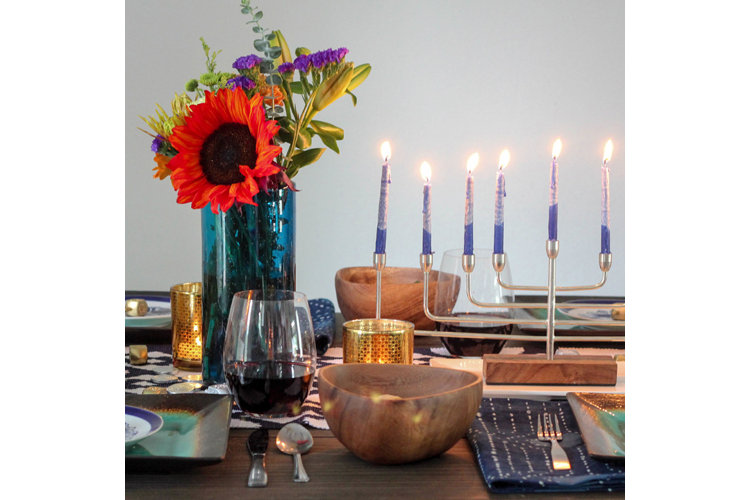 A modern Hanukkah dinner table with wood bowls, fresh flowers, and an ikat patterned table runner.