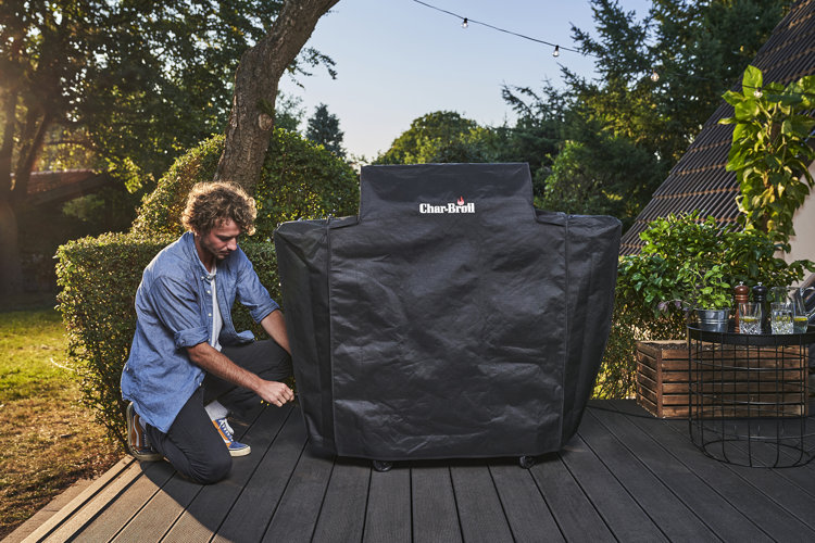 A man putting a grill cover on a grill outside on a patio