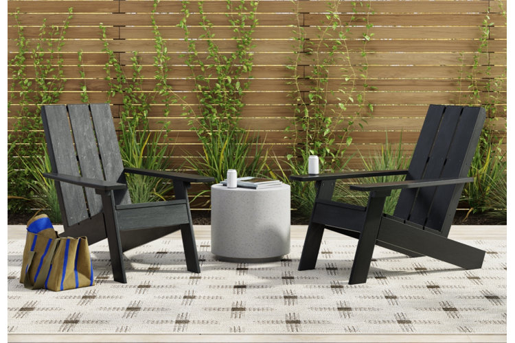 a pair of black wooden Adirondack chairs and a concrete end table on a patio with an outdoor geometric-print area rug
