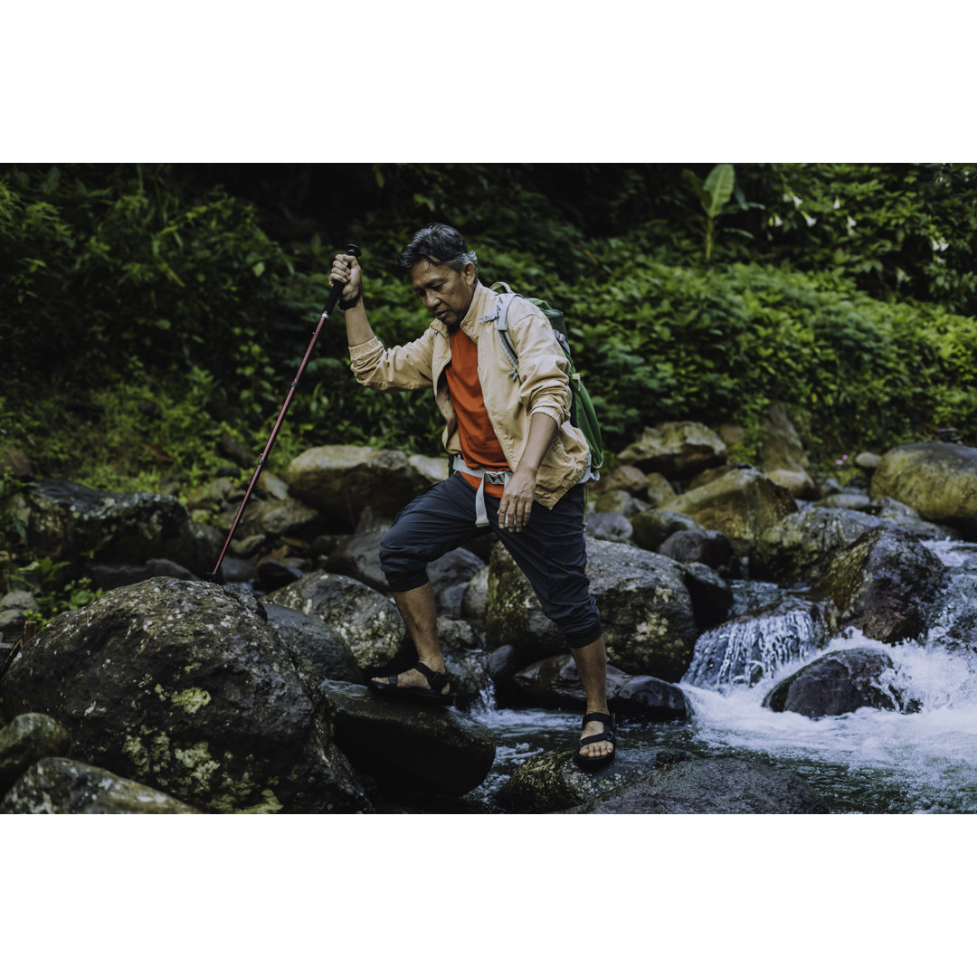 Zufriedener älterer männlicher Wanderer mit Trekkingstock beim Überqueren des Flusses