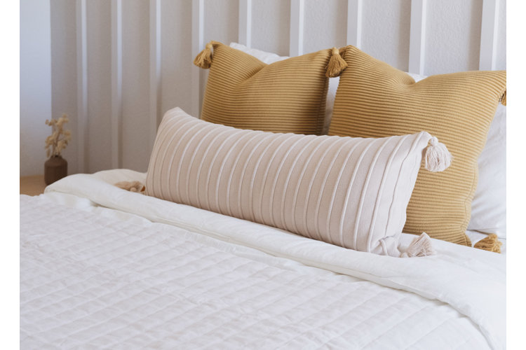 Full-size bed made up with cream bedding featuring two beige square pillows and a white tasseled lumbar pillow.