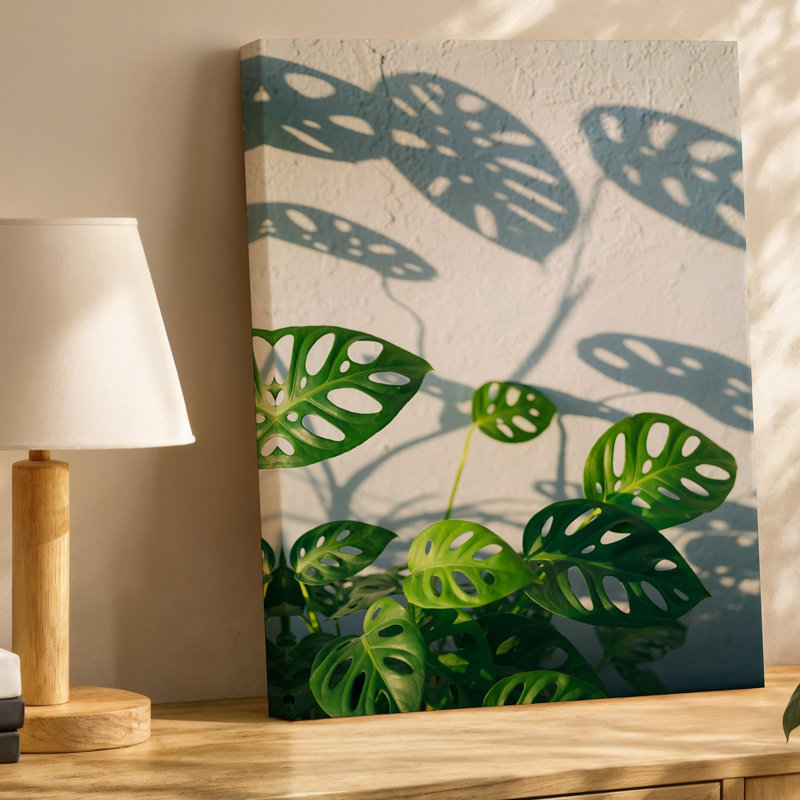 Toile, composition de gros plan avec grandes feuilles de Monstera lustrées, art mural positionné contre un mur blanc texturé à lumière douce