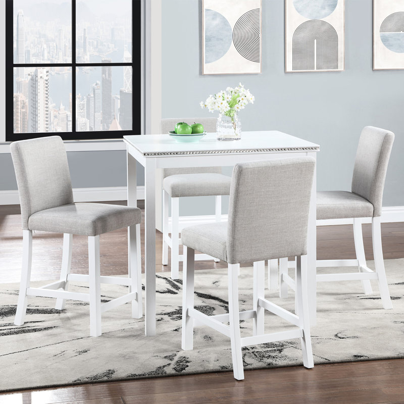 Ensemble table et chaises de salle à manger blanches, hauteur du comptoir, forme carrée avec broderie de cristal. Structure en bois massif. Quatre chaises blanches rembourrées.