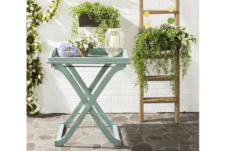 a blue wood butler table holding two potted plants and a candle inside a lantern