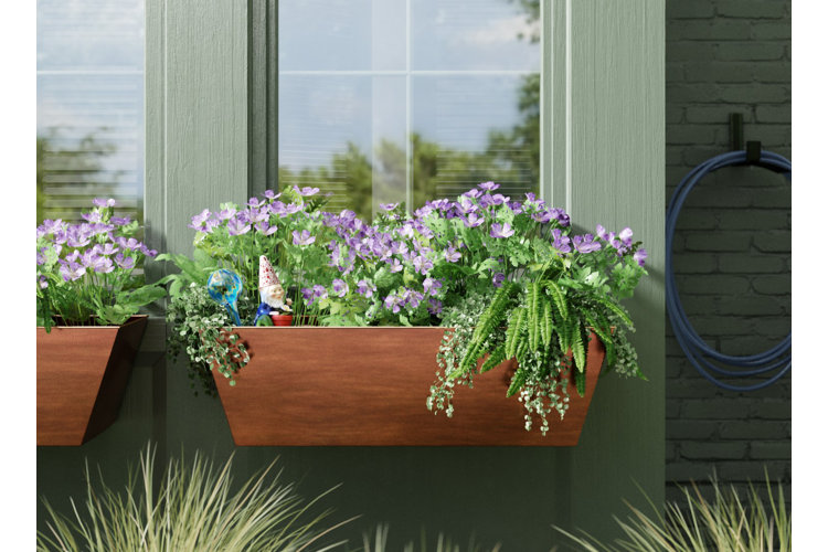 Copper metal window box planter installed beneath a window and planted up with purple flowers and ferns.