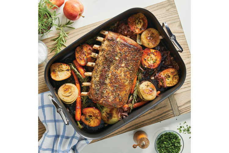 A close up of a rectangular cast iron roasting pan filled with roasted vegetables and a rack of lamb.