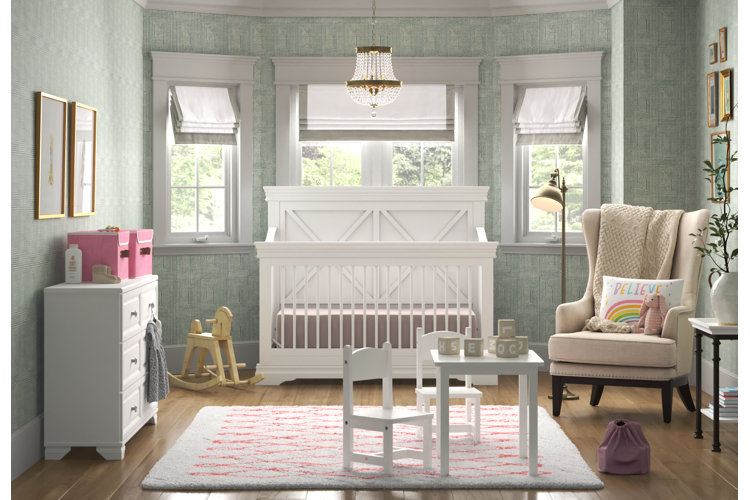 Blue nursery with chandelier over a white crib, white dresser, white plush area rug, and white table and chairs. Cream wingback accent chair on the wood floor. Yellow wood rocking horse