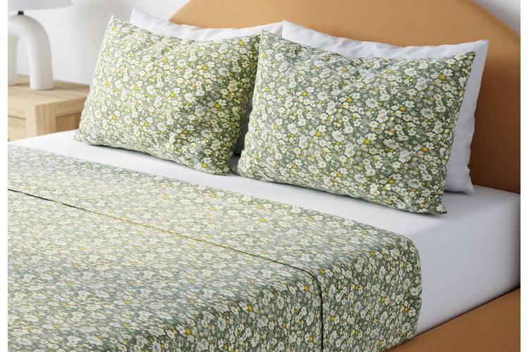 Orange upholstered bed with green floral bed sheets and matching pillows. White fitted sheet with matching white bed pillows behind the floral pillows