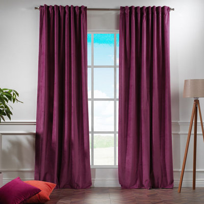 Two dark purple velvet curtains hanging on a rod over a window.