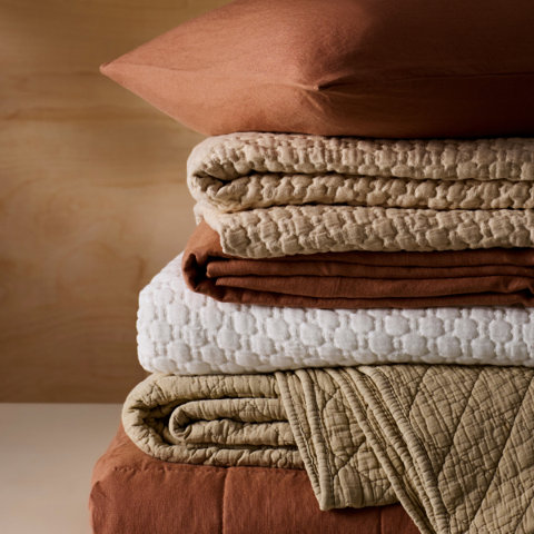 Stacked bed linens in brown, beige, and white colors.