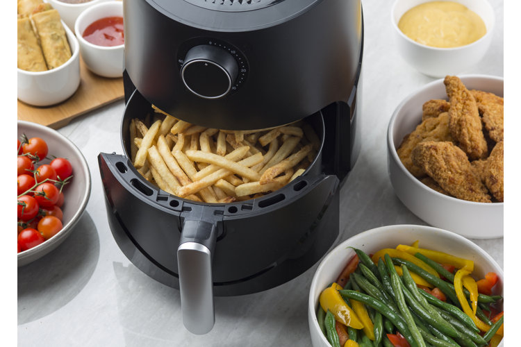 black air fryer with a basket of fries and surrounded by a range of fried and delicious foodds