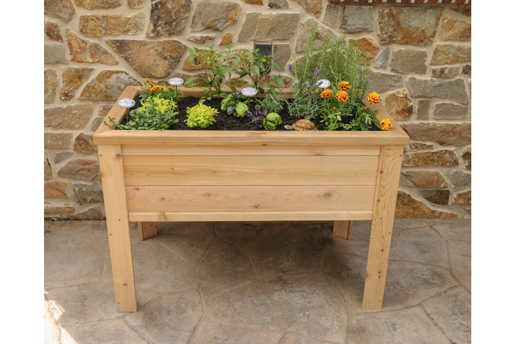 A wood elevated planter potted up with herbs and marigolds and placed up against a stone wall.