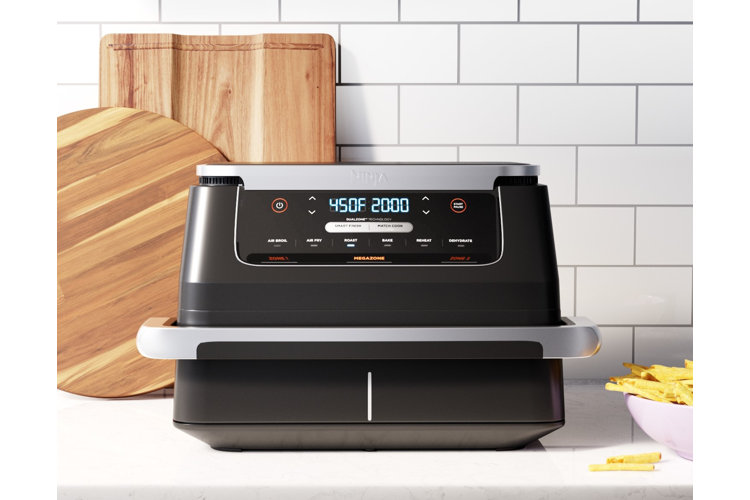 Large black air fryer on a counter beside a bowl of French fries and a pair of cutting boards.