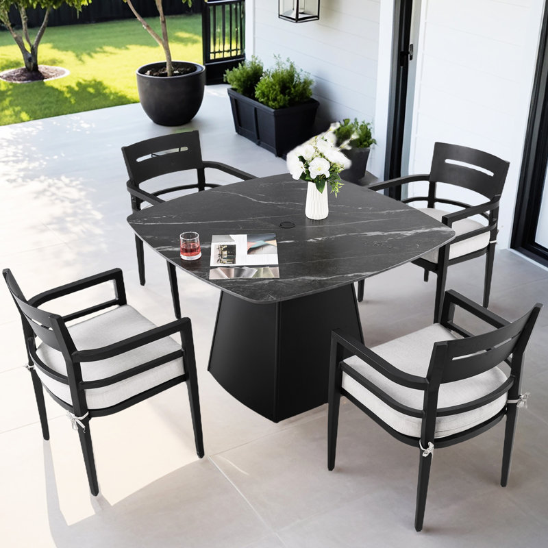 Ensemble de salle à manger d'extérieur 5 pièces, table en pierre frittée de 112 cm, fauteuils, coussins dégradés, patio moderne avec structure carrée arrondie et aspect rouille.