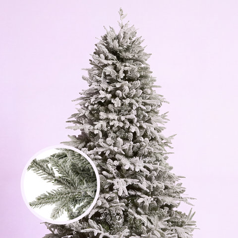 Flocked artificial Christmas tree with a detailed circular close-up view of the snowy, realistic needle texture against a light purple background.