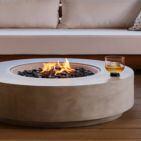 Round fire pit with glass and sofa in background.