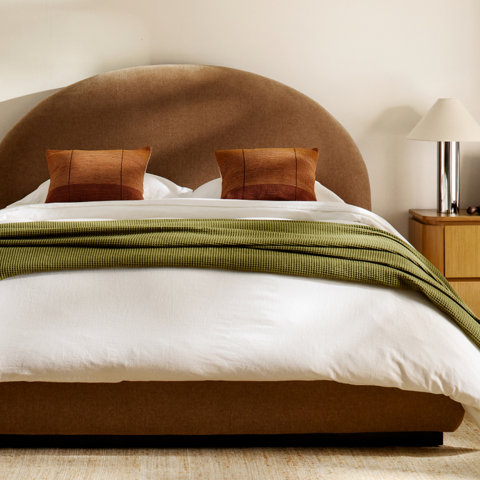 Bedroom with brown upholstered headboard, white sheets, green throw, and orange patterned pillows.