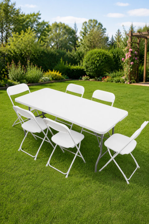 White rectangular folding table with six matching white folding chairs set up on a lush green lawn in a backyard.