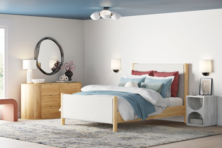 modern small bedroom with white walls and blue ceiling light wood modern dresser and bed white, orange, and blue bedding, white semi-flush mount ceiling light, white table lamp and