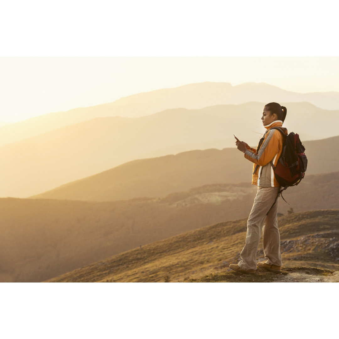 Backpacker mit Smartphone auf dem Berggipfel stehend