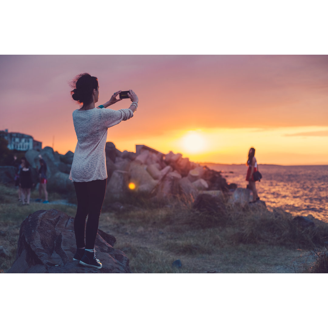 Frau am Strand beim Fotografieren des Sonnenuntergangs