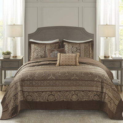 Grand couvre-lit réversible - 5 pièces. Brun et or. Comprend un couvre-lit, 2 taies décoratives et des coussins décoratifs. Fabriqué à partir d'amende pour un luxe durable. Expositions de feuilles, rayures, motifs. Décoré avec des coutures.