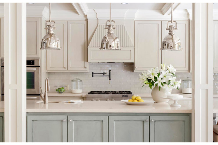 Cream colored and sage green kitchen with silver pendant lights and a black pot filler over the stove