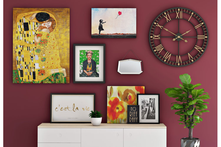 gallery wall of impressionist artwork and a metal wall clock on a maroon wall above a console table