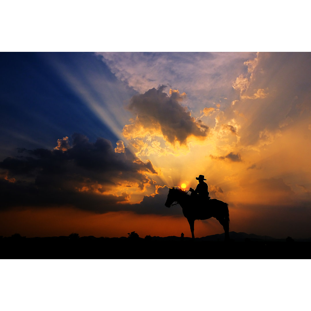 Leinwandbild Die Silhouette eines Cowboys zu Pferd bei Sonnenuntergang vor einem Hintergrund