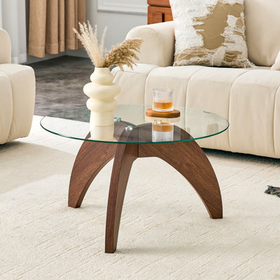 Table basse ronde à pieds triangulaires de style créatif, d'environ 27,5 pouces de diamètre, avec plateau en verre trempé transparent et panneau de fibres à densité moyenne de couleur noyer. Parfait comme table basse de salon, etc.