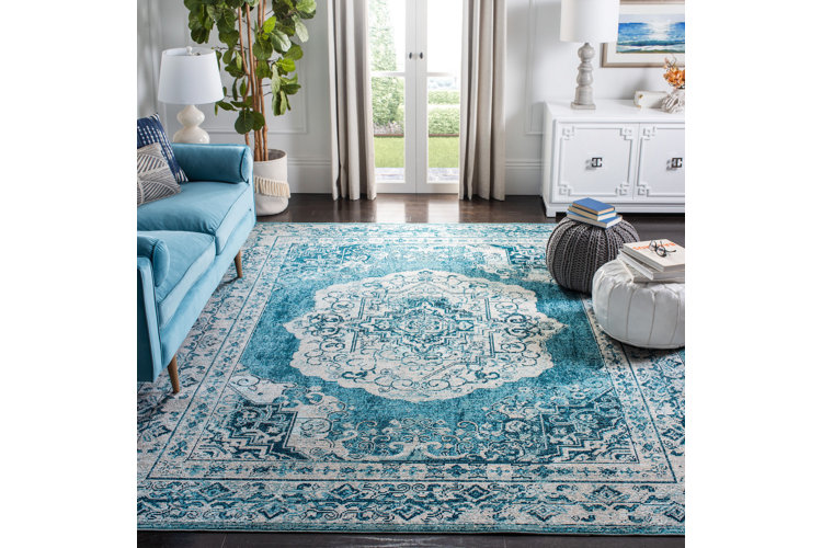 Living room with a blue patterned area rug, blue sofa, and neutral pouf ottomans.