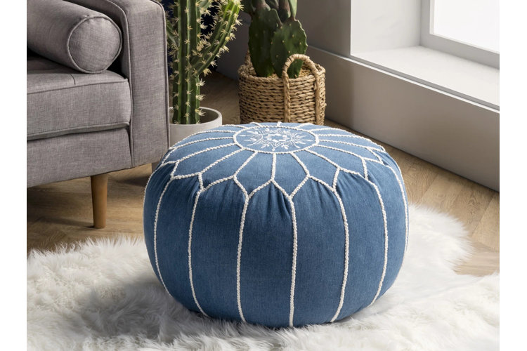 Round blue Moroccan pouf with a white embroidered design on top of a faux sheepskin rug.