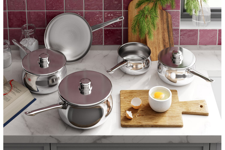 Kitchen counter with a stainless steel cookware set next to a wood cutting board on the counter and two wood cutting board leaning against the wall
