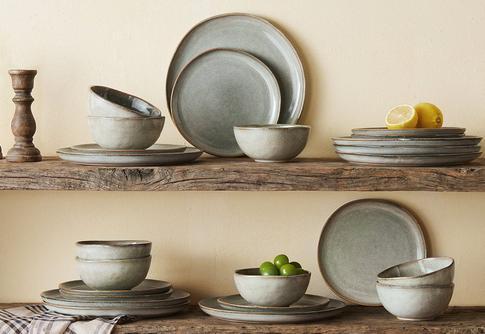 Rustic sage green dinnerware set with reactive glaze finish displayed on reclaimed wood shelves with lemons and grapes.
