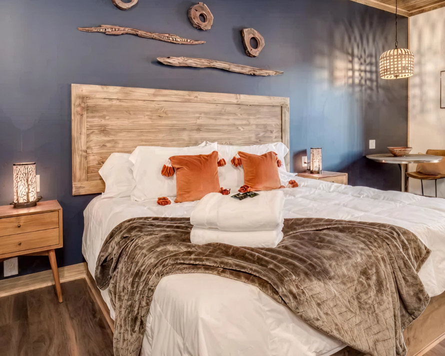 Boutique hotel bedroom with a wood headboard, driftwood wall art, and orange accent pillows