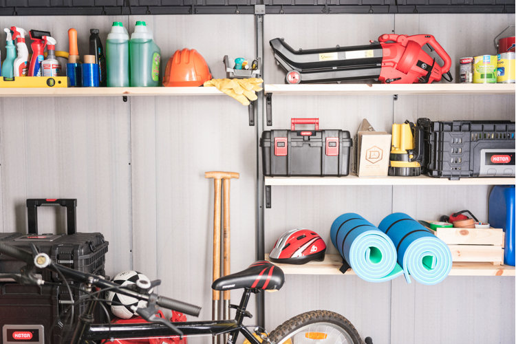 Close up of wall-mounted garage shelves used to store cleaning supplies, tools, and bike-riding equipment.