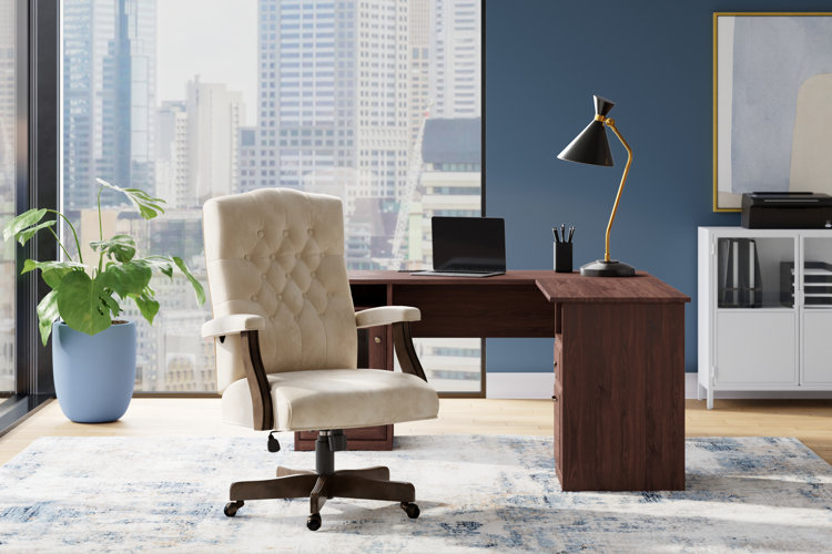 luxury home office wooden l shape desk and ergonomic upholstered desk chair with black desk lamp and plant in corner
